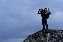 Photographer, Vincent Munier, standing on large rock looking through binoculars, Forollhogna National Park, Norway, September 2008