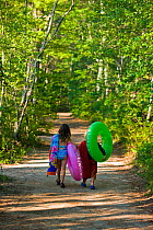 Children in swimming costumes and with inflatables walking to the beach along a woodland road, White Lake State Park in Tamworth, New Hampshire, USA. October 2009
