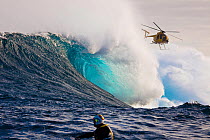 Helicopter filming a tow-in surfer at Peahi (Jaws) off Maui, Hawaii. Man in foreground is driving a jetski.