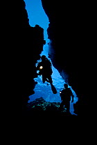 Divers with lights entering Second Cathedral through the upper crack in the ceiling, off the Island of Lanai, Hawaii. Model released.