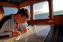 Fishing skipper doing chartwork in the wheelhouse of his trawler. February 2010, Model released.