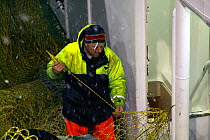 Trawlerman repairing nets on a snowy February night on the North Sea, 2010. Model released.