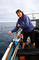 Woman fishing for mackrel and pollack with a hand line from a small motorboat (Orkney Longliner), Eastern Isles, Isles of Scilly, UK. Model Released.