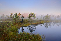 Misty morning with reflections on lake, hiker taking photographs,  Estonia