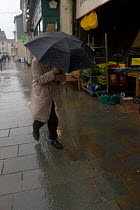 Man using umbrella as shield against rain in storm. Example of impact of climate change on ordinary people. Denbigh, North Wales, UK. July 2009.