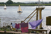 Woman pauses  from hanging washing, to watch the bore and pleasure craft. Severn Estuary. England, August 2009