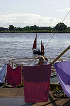 Woman hanging her washing, pauses to watch the bore and pleasure craft. Severn Estuary. England, August 2009