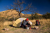 Hiker cooking beside his tent, at winter campsite in the Tumacacori Mountains of the Coronado National Forest. Arizona, USA, March 2009, model released