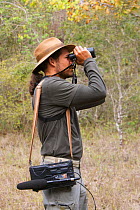 Local guide with recording equipment, looking through binoculars, birdwatching in the Pantanal, Brazil. Model Released.