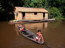 Children in a canoe beside their house made of Babassu straw (Orbygnia phalerata) in the Amazon Upland Rainforest, Ayapua community, Piagacu-Purus Sustainable Development Reserve, Ayapua Lake of Pur...