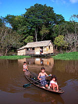 Children in a canoe beside their house made of babassu straw (Orbygnia phalerata) in the Amazon Upland Rainforest, Ayapua community, Piagacu-Purus Sustainable Development Reserve, Ayapua Lake of Pur...