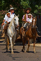 Three generations of traditionally dressed gauchos (cowboys) riding horses (Equus caballus) during the parade of the Fiesta De La Patria Gaucha, Tacuarembo, Uruguay, April 2008