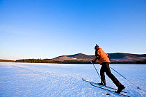 Man cross-country skiing on First West Branch Pond with White Cap Mountain is in the distance. Greenville, Maine, USA, March 2009, Model released.