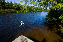 Boy playing on rope swing over the Androscoggin River, Mollidgewock State Park in Errol, New Hampshire. USA, August 2008. Model released.