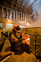 Man stoking the fire in the sap evaporator of the sugar house at Sugarbush Farm in Woodstock, Vermont, USA, April 2008.
