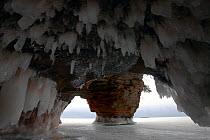 Ice hanging from arch in sea cave carved in soft sandstone cliffs, framing sea stack and frozen lake, Squaw Bay, Lake Superior, Apostle Islands National Lakeshore, Wisconsin, USA, February 2009