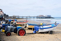 Traditional Cromer crab boats with tractors on beach, with pier in background, UK, October 2009