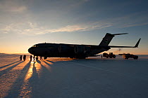Equipment being unloaded from aeroplane, US Military C17 Globemaster, on the frozen sea ice, McMurdo Sound, Ross Sea, Antarctica, sunset.
