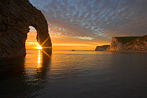 Sun setting through the arch at Durdle Door, Dorset, England, UK. Jurassic Coast World Heritage Site, March 2009