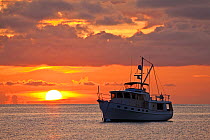 Sun setting behind motorboat anchored in the Exumas, Bahamas, Caribbean, June 2009.