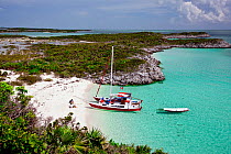 30ft Tiki catamaran "Abaco" anchored in secluded cove in the Exumas, with people sat on the beach. Bahamas, Caribbean. June 2009. Property and model released.