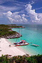 30ft Tiki catamaran "Abaco" anchored in secluded cove in the Exumas, with people sat on the beach. Bahamas, Caribbean. June 2009. Property and model released.