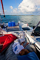 Boy sleeping on deck of 30ft Tiki catamaran "Abaco". Exumas, Bahamas, Caribbean. June 2009, Model and property released.