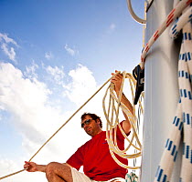 Man gathering up sheet, sailing in the Grenadines, Caribbean. February 2010. Model released.