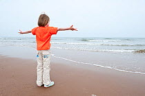 Young girl dancing on a beach, arms open wide towards the sea, Scotland, UK, June 2009. Model released