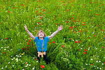 Young girl arms in air, waving / playing in a wildflower meadow, Scotland, UK, July 2009. Model released