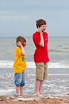 Children on a beach with cell phone and 'shell phone' Scotland, UK. Model released