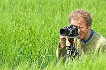 Portrait of camerman Tim Shepherd, taking stills for the BBC in a Wheat field, UK, June 2007