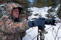 Portrait of photograher Jim Brandenburg in camouflage jacket, setting up timelapse function on stills camera, Secret Bay, Minnesota,  USA, March 2008
