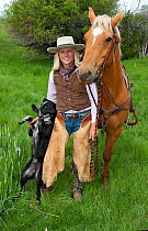 Cowgirl with Palomino horse (Equus caballus) and ranch dog in field, Colorado, USA, North America. June 2009. Model released
