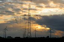 Electricity cables, pylons and wind turbines at sunset. Near Diepholz, Lower Saxony, Germany.