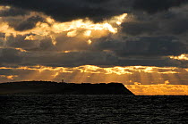 Stormy sky over Hiddensee island with flashing lighthouse and Baltic sea at sunset. Viewed from Rugen island, Mecklenberg-Vorpommern, Germany.