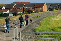 Three people walking alongside Severn estuary on coastal footpath. Gloucestershire, England, UK April 2010