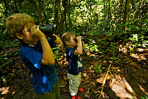 Young brother and sister (both model released) exploring tropical rainforest and looking through binoculars, Danum Valley Conservation Area, Sabah, Borneo, Malaysia, July 2007