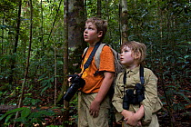 Two young children (brother and sister- model released) in tropical rainforest watching a wild orangutan. Borneo, July 2007