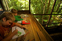 Two young children (brother and sister-model released) working on their journals at a research station in tropical rainforest, Borneo. July 2007