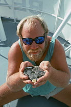 Man holds up gold and silver Doubloons recovered from the shipwreck "Las Maravillas", a Spanish galleon sunk in 1658, Bahamas. 1987 Model released.