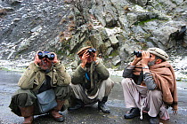 Local scouts looking through binoculars for Snow leopard (Panthera unicia) Chitral, in the Hindu Kush mountains, North West frontier, Pakistan. For BBC Planet Earth series, 2005.