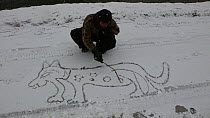 Member of film crew entertains himself by drawing Snow leopard in the snow while crew searches for animals to film for BBC Planet Earth series, Mountains episode, Chitral, Hindu Kush, Pakistan 2005