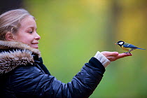 Great tit (Parus major) feeding from  young girl's hand in an urban park. Paris, France, November 2009.