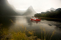 An excursion boat passing through a misty view of Mitre Peak in Milford Sound, a World Heritage Site, in Fjordland on the South Island of New Zealand. January 2008.