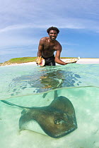 Split level image of Tour guide with fresh conch salad lunch and stingray (Dasyatis americana) on Gibbs Cay, Grand Turk, Turks and Caicos, Caribbean. June 2007. (model released)