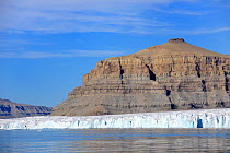 Iceberg and glacier, with striated sedimentary cliffs of coastline behind, Croker Bay, Devon Island, Nunavut, Canada,  August 2010