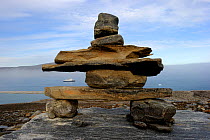 A traditional Inukshuk sculpture in figurative form, on the coast of Sunshine Fjord, with a cruise ship behind, Nunavut, Canada, August 2010