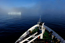 View from deck of a cruise ship cruising along Baffin Island with an iceberg emerging out ot the mist, Nunavut, Canada, August 2010