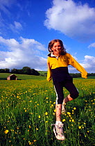 Girl running through Buttercup (Ranunculus) meadow, UK